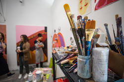 Painting studio with brushes, art on walls, and people