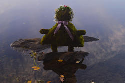 figure in wood and moss protruding from dark lake