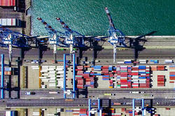 an overhead view of dozens of shipping containers on a long barge at sea