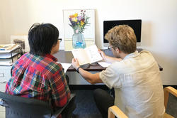 two students sitting next to each other in an office setting, as they review the content of a book