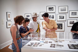 Students at the RISD Museum looking at a display case of photos, with exhibition walls displaying framed photographs in the background