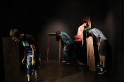 people in a dark room standing in a listening posture next to wooden structures