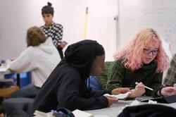 Two students working together, in the foreground, while Associate Professor Paula Gaetano-Adi speaks to a student in the background