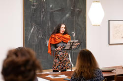 Latinx student in orange scarf giving a poetry reading.