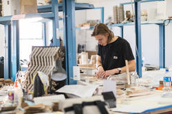 architecture student works on a model in a room surrounded by art materials