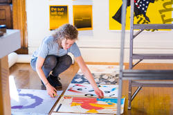 student is placing different prints onto the ground in a studio space