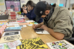 Students sit around a table full of zines at Queer Archive Works and draw