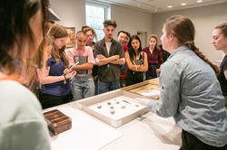 students gather around a table of museum objects as a curator speaks to them