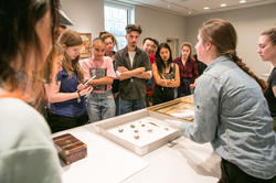 students gather around a table of museum objects as a curator speaks to them