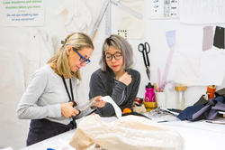 a Rhode Island School of Design Apparel Design faculty member cuts fabric as a student looks on