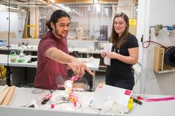 two students in an industrial design studio observe and discuss work in progress