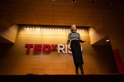 Amy Devers, host of the event, stands on stage in the Chase Auditorium with the TEDxRISD sign behind her