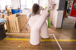 a student shapes a pinkish-white abstract sculpture in a large, industrial studio space
