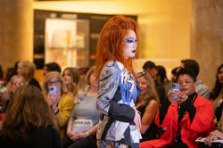 A model walks down the runway in drag and a red with in a garment made by Disco Amber