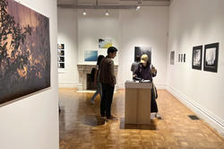 Visitors look through Ethan Brossard's photo book in the woods gerry-gallery on opening night of the 2023 photography triennial