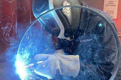 sparks fly as an artist in protective head gear welds a metal ring