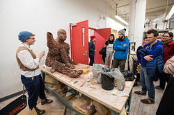 A group of people are gathered around a worktable where a sculpture is in progress.