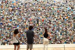 Three people stand facing a wall of hundreds of colorful photographs