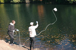 faculty member Max Pratt throws a sample-collecting bucket into the Blackstone River