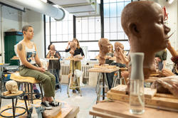 students surround the live model as they put the finishing touches on their portraits in clay