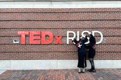 Two people hand up TEDxRISD lettering