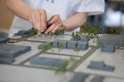 a student glues miniature trees to a large 3D model of a site in Detroit
