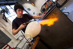 a Glass student uses a blowtorch to shape a glass vessel