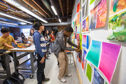 an Illustration student pins work on a wall during a studio crit