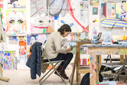 student sitting in a chair focused intently on their painting