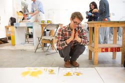 Student squatting and rolling yellow clay with their hands