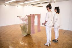 Student work by Emily Holtzman BFA 2018. Two students viewing fabric art suspended from the ceiling on wires and wooden poles.