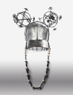 Student artwork featuring a silver hat with two flower covered silver orbs on the top and an attached necklace 