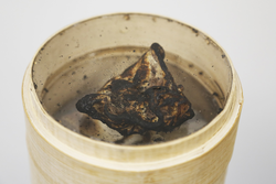 Closeup image of a charred dumpling in a bamboo steamer