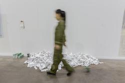 Art piece by Zhang Yi, MFA 2016. A woman walks by a large pile of printed paper strips.