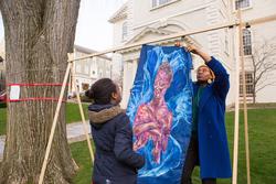 Students hanging up a portrait painte on large fabric