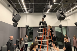 RISD students standing on ladders stage a performance for a small audience inside the Spatial Audio Studio