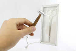 a hand holds a silver-headed hammer close to a glass case containing a pair of scissors