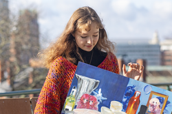 RISD Student in a colorful sweater and black turtleneck holding a brightly colored still life painting  