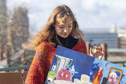 RISD Student in a colorful sweater and black turtleneck holding a brightly colored still life painting