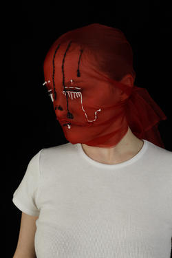 a model wears a red sheer scarf, covering her head, with white and black patterns stitched in, designed by Eleanor Kutzer