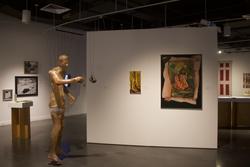a life-sized adult human marionette among paintings and other works in a gallery
