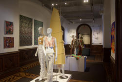 several mannequins decorated with apparel designs on display in a gallery hallways, surrounded by walls adorned with artworks