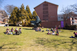 Several circles of RISD students sit on either side of a modernist sculpture, on the stretch of lawn known as the RISD Beach
