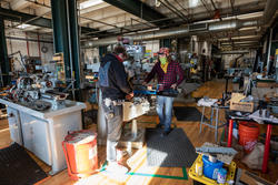 Two students with face coverings work inside the Industrial Design metal/machine shop