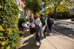 Several students carry art supplies on walk up College Hill