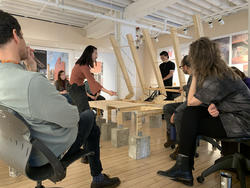 a R I S D student displays a wooden structure to faculty and other students inside a studio classroom