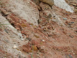 a bed of multicolored rocks sitting inside a reddish clay deposit atop a rock wall