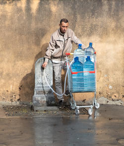 a person stands against a tan wall as they pump water into larger blue containers inside a cart