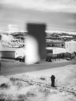 black and white photo of industrial buildings in a desolate area with mountains in the background and a small human figure in the foreground