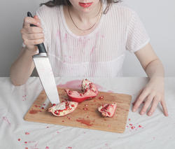 a person in a white shirt stabs at a pomegranate as they drool a stream of red liquid, the rest of their head out of frame
